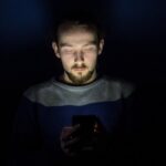 暗がりでスマホを見つめる男性