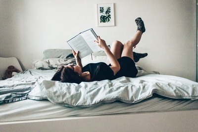 人＿ベッドに仰向けになって本を読む女性